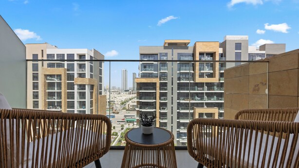 Un balcon avec des fauteuils en osier, une petite table et une vue sur des immeubles modernes.