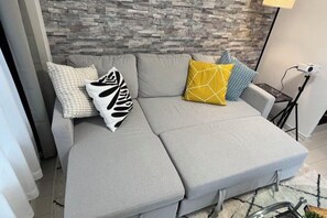 A grey sofa with a geometric patterned pillow, a yellow pillow, and a blue pillow with a leaf design. - Relax House (Tokyo)
