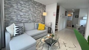 A modern living room with a grey sofa, a glass coffee table, and a stone-patterned wall. - Relax House (Tokyo)