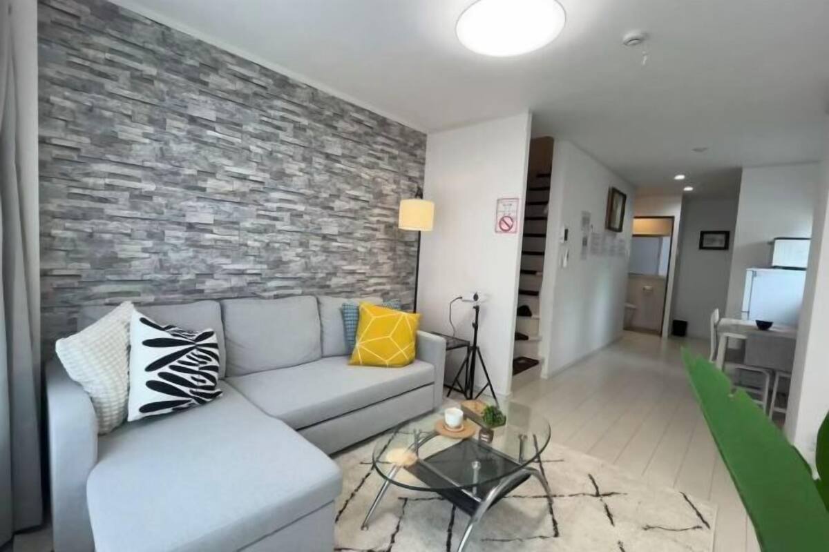 A modern living room with a grey sofa, a glass coffee table, and a stone-patterned wall.