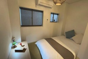A small, neatly arranged bedroom with a bed, bedside table, and two windows. - Relax House (Tokyo)