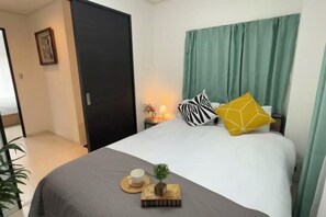 A hotel room with a bed, a nightstand, a small plant, and a cup on the bed. - Relax House (Tokyo)