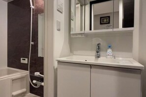 A bathroom with a white sink, a mirror, a shower enclosure, and a cabinet. - Relax House (Tokyo)
