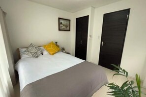 A bedroom with a bed, a nightstand, a plant, and two doors. - Relax House (Tokyo)