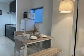 Un'area pranzo con un tavolo apparecchiato per due, un forno a microonde sopra un frigorifero e una lampada a parete.