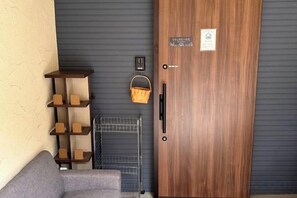 A wooden door with a handle and a small sign, a metal rack with baskets, and a gray sofa against a textured wall. - Relax House (Tokyo)