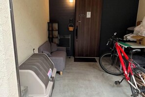 A compact room with a sofa, a bicycle, and a door to a dark room. - Relax House (Tokyo)