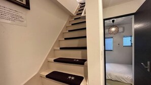 A staircase with black steps and white walls, leading to a room with a bed and a hanging light fixture. - Relax House (Tokyo)