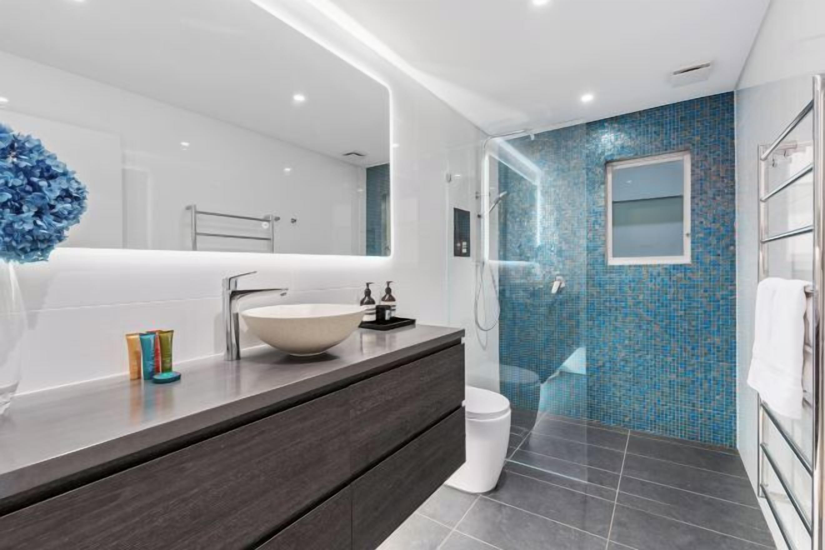 A modern bathroom with a large mirror, a vessel sink, a glass shower enclosure, and a tiled floor.