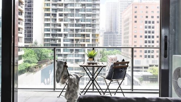 A balcony with a view of high-rise buildings, a small table with a plant, and two chairs. - A Spacious 2BR Apt, Walk to Southern Cross Station (Melbourne)