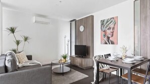 A modern living room with a sofa, coffee table, TV, and dining area with chairs and a table. - A Spacious 2BR Apt, Walk to Southern Cross Station (Melbourne)