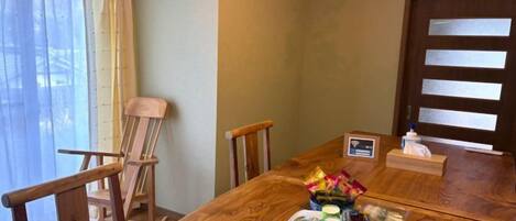 Una mesa de madera para comer con una bandeja de objetos, una silla de madera y una ventana con cortinas.