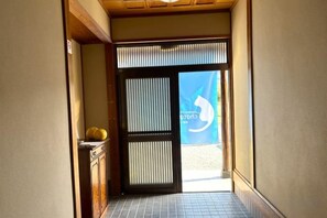 Un couloir mène à une pièce dotée d’une porte coulissante, d’un sol carrelé et d’une petite armoire contenant un panier de fruits.