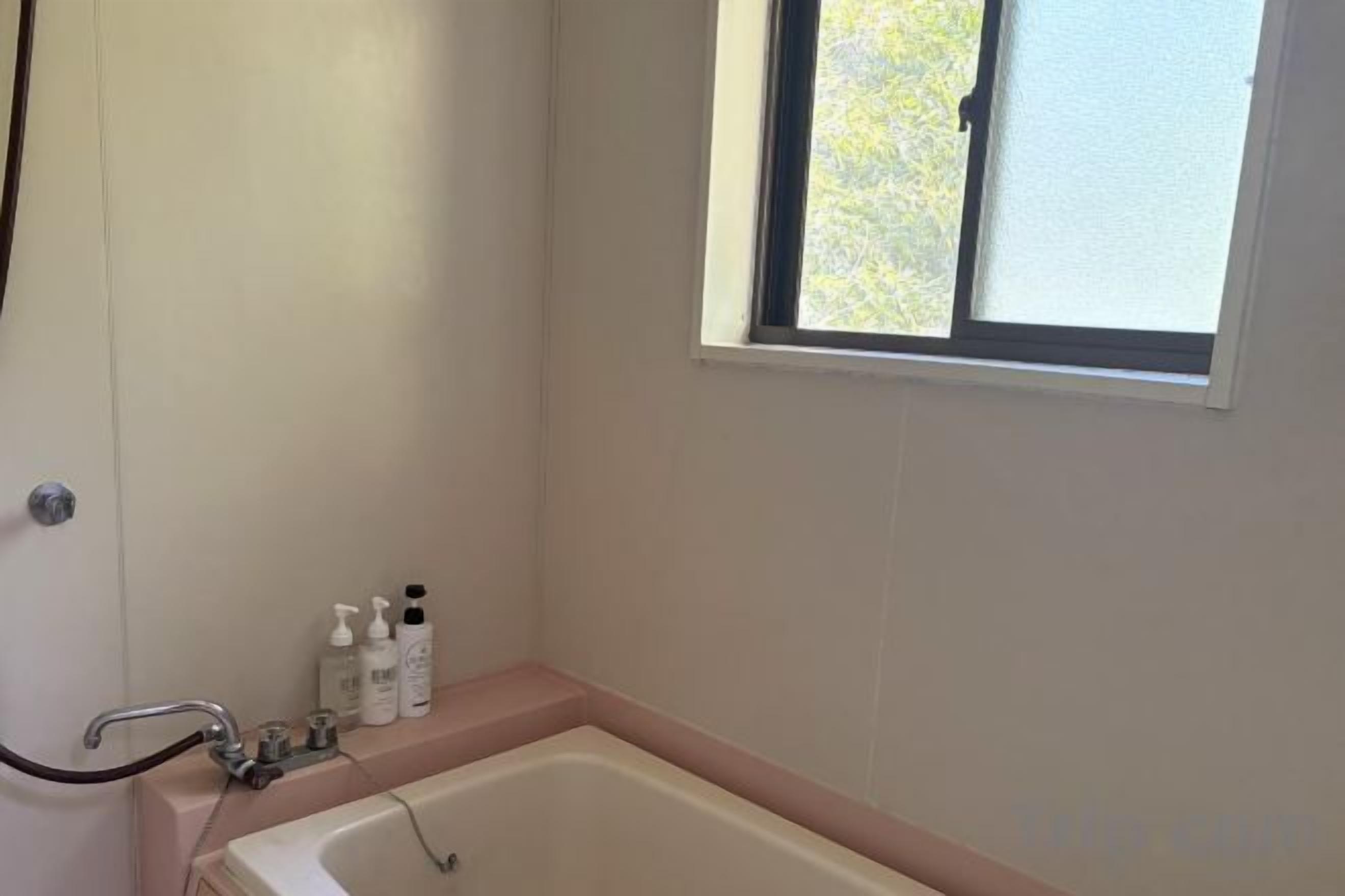 A bathroom with a bathtub, a window, and toiletries on the counter.
