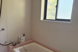 A bathroom with a bathtub, a window, and toiletries on the counter. - chambre d'hôte chaton (Taiki)