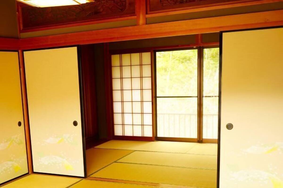 A traditional Japanese room with tatami flooring, sliding doors, and a view of greenery outside.