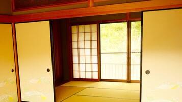 A traditional Japanese room with tatami flooring, sliding doors, and a view of greenery outside.