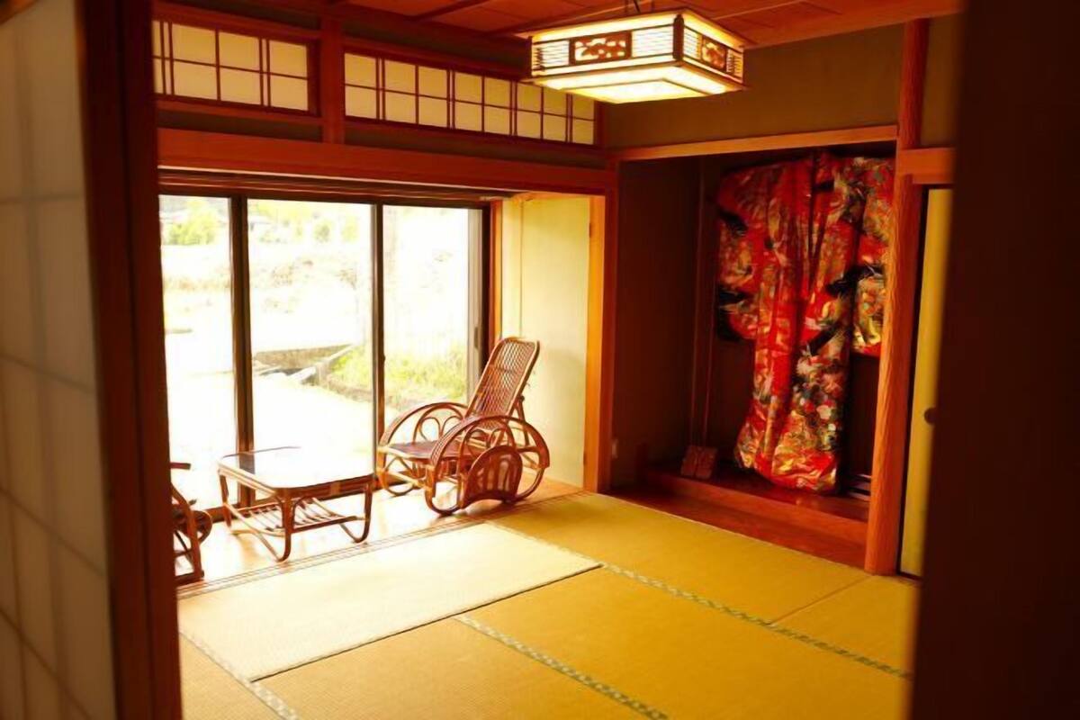 A traditional Japanese room with tatami flooring, a low table with a chair, and a sliding door with a floral curtain.