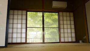 A traditional Japanese room with tatami flooring, sliding doors with shoji screens, and a view of greenery outside. - chambre d'hôte chaton (Taiki)
