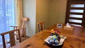 A wooden dining table with a tray of items, a wooden chair, and a window with curtains. - chambre d'hôte chaton (Taiki)