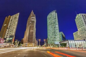 Un paisaje urbano nocturno con modernos edificios de gran altura, una calle ancha y estelas de luz dejadas por vehículos en movimiento.