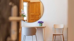Une pièce avec une porte en bois, un miroir rond, une petite table sur laquelle est posé un vase de fleurs et deux chaises.