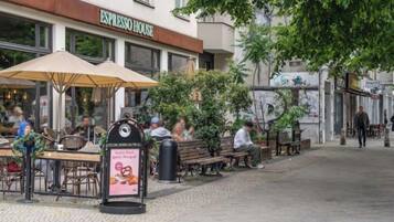 Ein Außenbereich mit Tischen und Sonnenschirmen, ein Schild für ESPRESSO HOUSE und ein Fußweg.