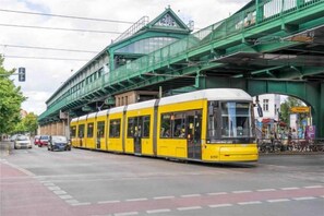 Un tram jaune se trouve à une station, avec un pont vert qui passe au-dessus.