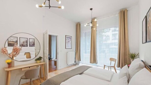 Une chambre d’hôtel moderne avec un grand lit, un bureau avec une chaise, un grand miroir rond et une vue sur la ville grâce à de larges fenêtres.