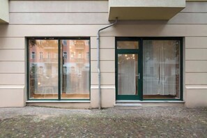 Une façade d’immeuble avec de grandes fenêtres et une porte, une petite marche menant à l’entrée et un sol pavé.