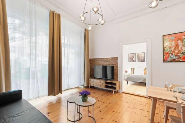 Una sala de estar moderna con un sofá, una mesa de centro con flores, un televisor y un comedor con una mesa y sillas.