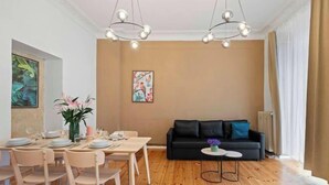 Un coin repas avec une table et des chaises en bois, un canapé noir et une petite table d’appoint sur laquelle est posé un vase.