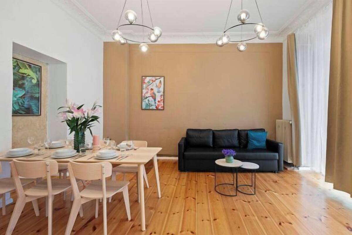Un coin repas avec une table et des chaises en bois, un canapé noir et une petite table d’appoint sur laquelle est posé un vase.