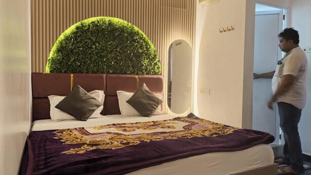 A hotel room with a bed, a large mirror, a green circular wall decoration, and a person standing by the door. - Shiv Kashi Paying Guest House (Varanasi)