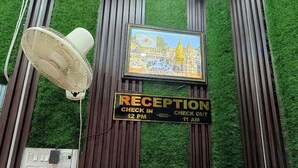 A reception area with a check-in/out sign, a fan, and a framed picture on the wall. - Shiv Kashi Paying Guest House (Varanasi)