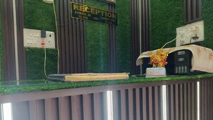 A reception desk with a green artificial grass wall, a sign indicating check-in and check-out times, and a statue on top. - Shiv Kashi Paying Guest House (Varanasi)