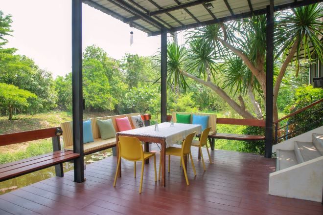 Un espace extérieur aménagé, couvert et doté de tables et de chaises, entouré d’une végétation luxuriante et d’une terrasse en bois.