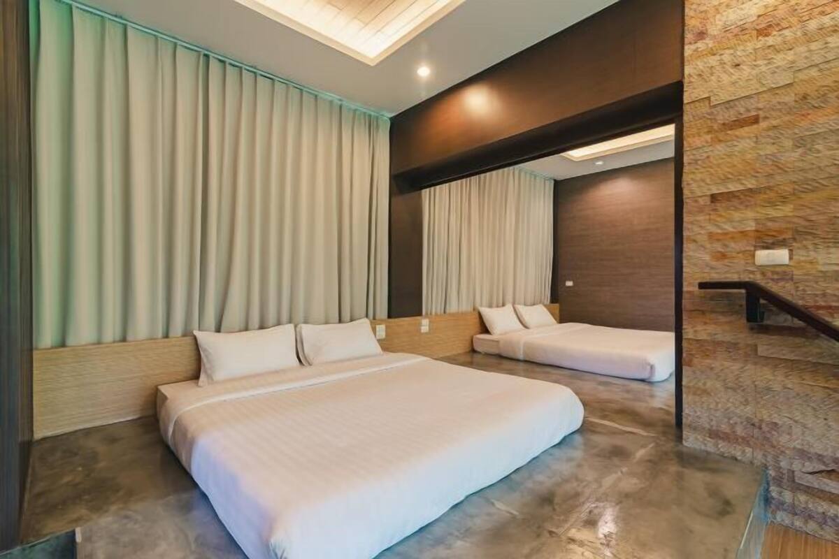 A hotel room with two beds, a large window with curtains, a wooden headboard, and a stone accent wall.