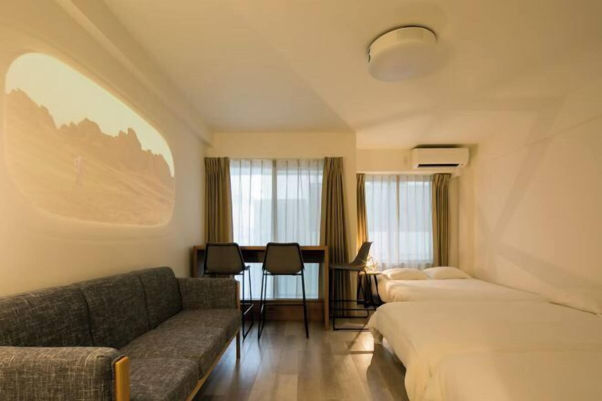 Ein Hotelzimmer mit einer Couch, einem Bett, einem Schreibtisch mit Stühlen und einem großen Fenster mit Vorhängen.