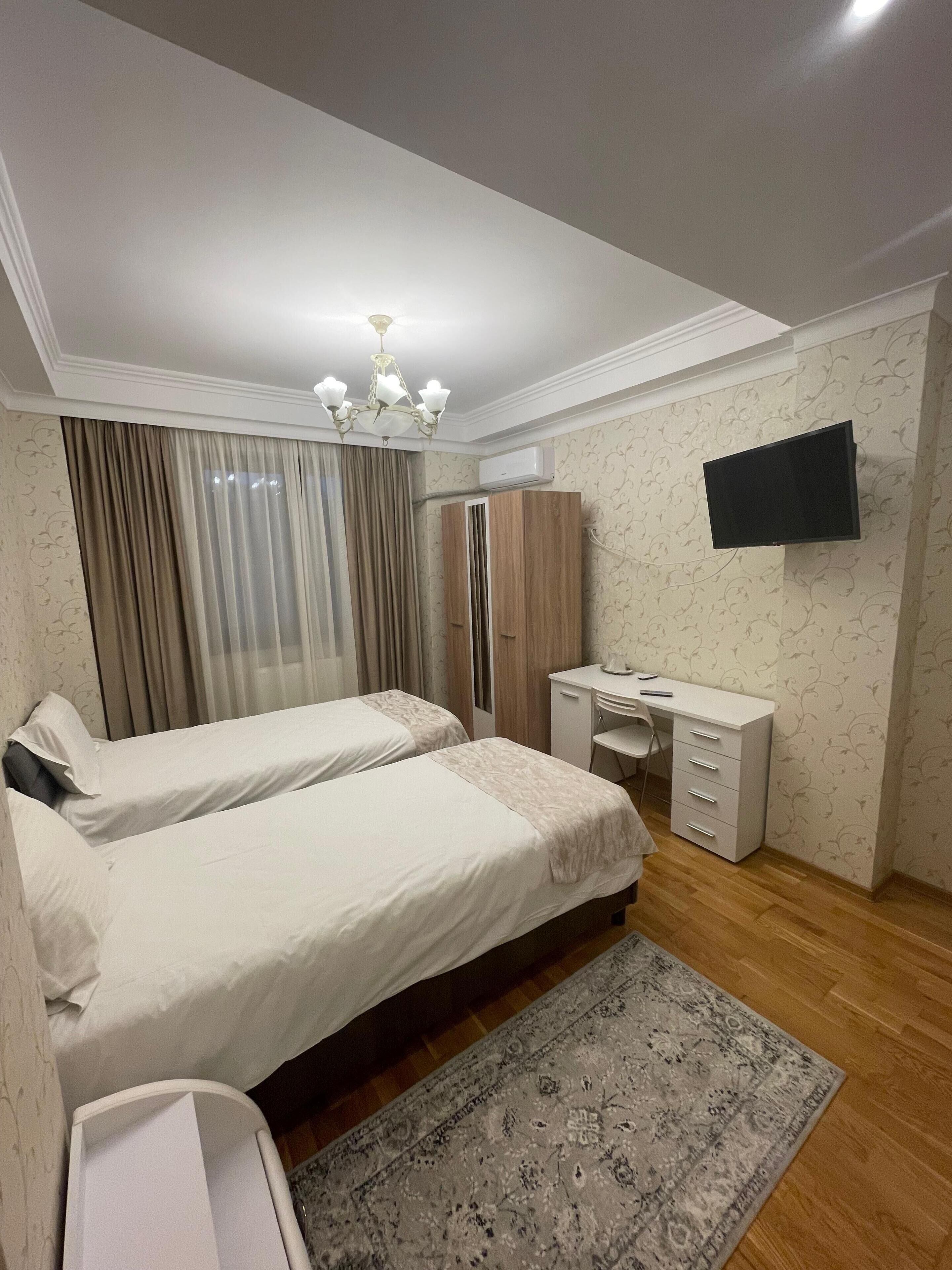 Une chambre d’hôtel avec deux lits, un bureau, une chaise, une télévision et un tapis à motifs.