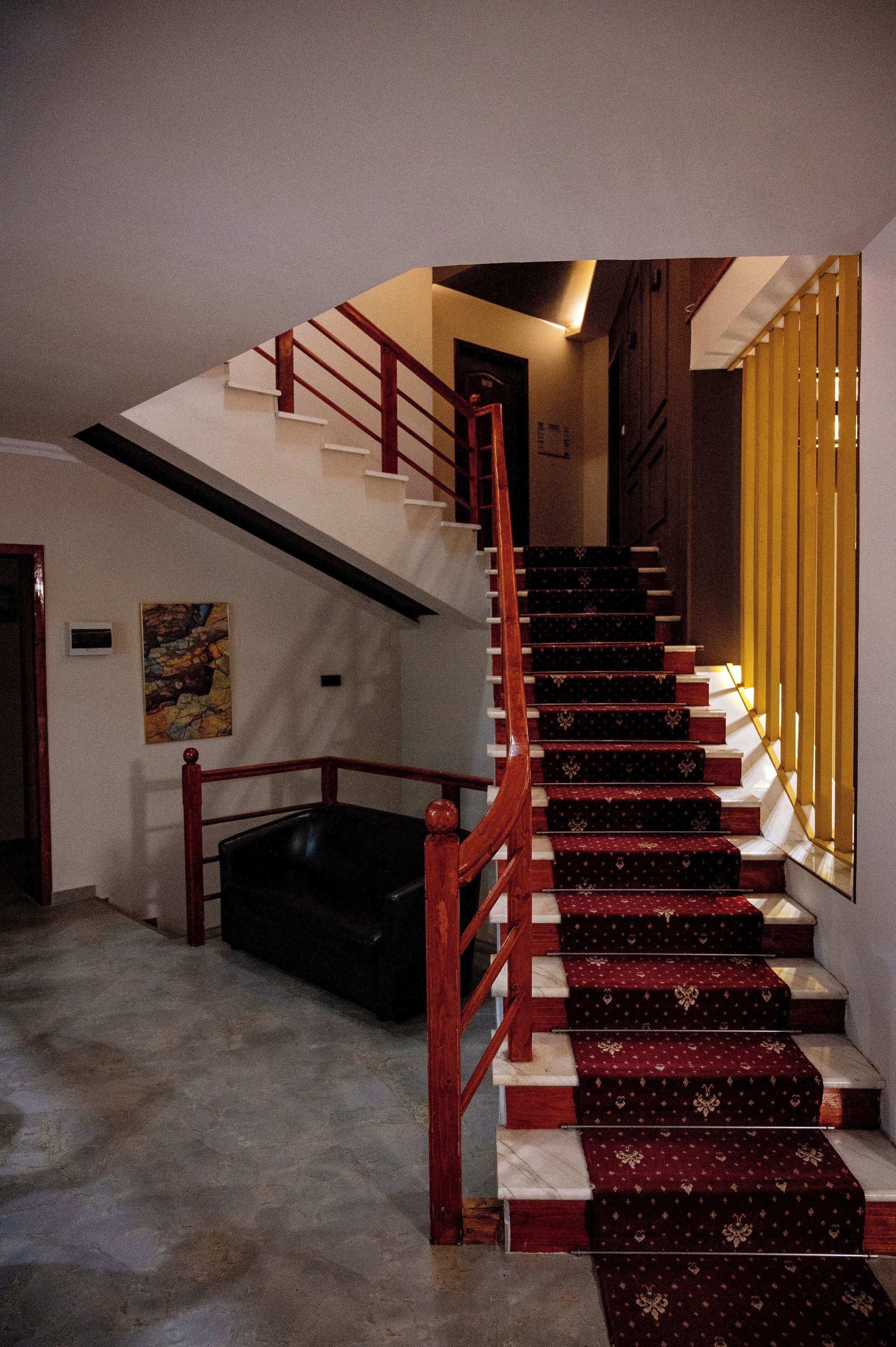 A staircase with a red handrail and patterned carpet, leading to a landing with a black leather couch.