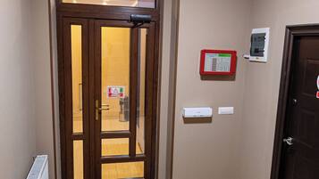 A hotel entrance with a brown door, a glass door, a sign indicating an exit, a fire alarm, and a radiator.