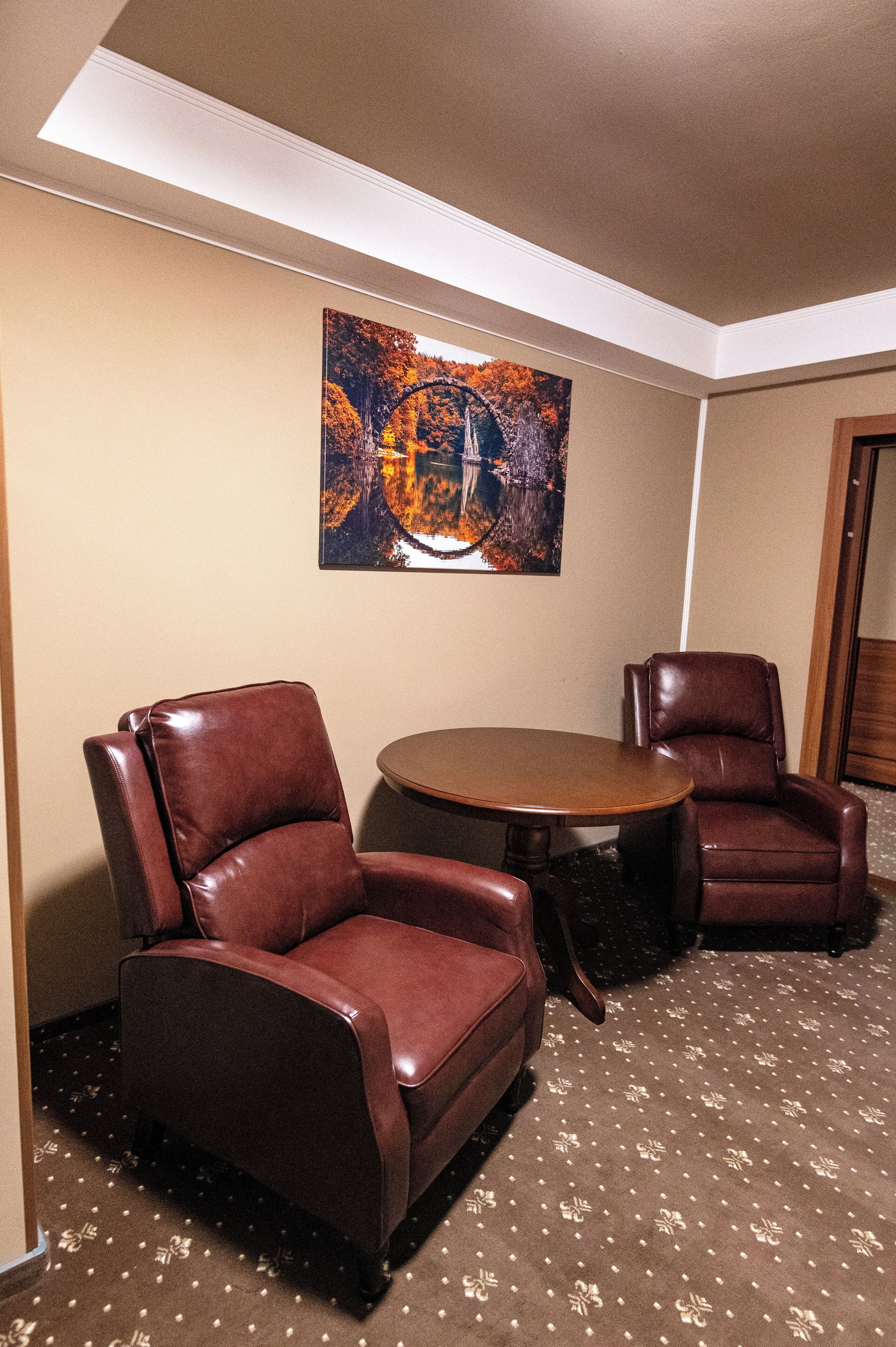 A room with two leather chairs, a round table, and a painting on the wall.
