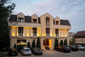 A multi-story hotel with a symmetrical facade, multiple balconies, and a parking area with several cars. - Pensiunea Crystal (Rediu)