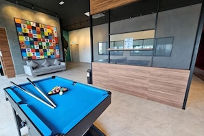 A pool table in a modern room with a gray sofa and a colorful abstract wall art.