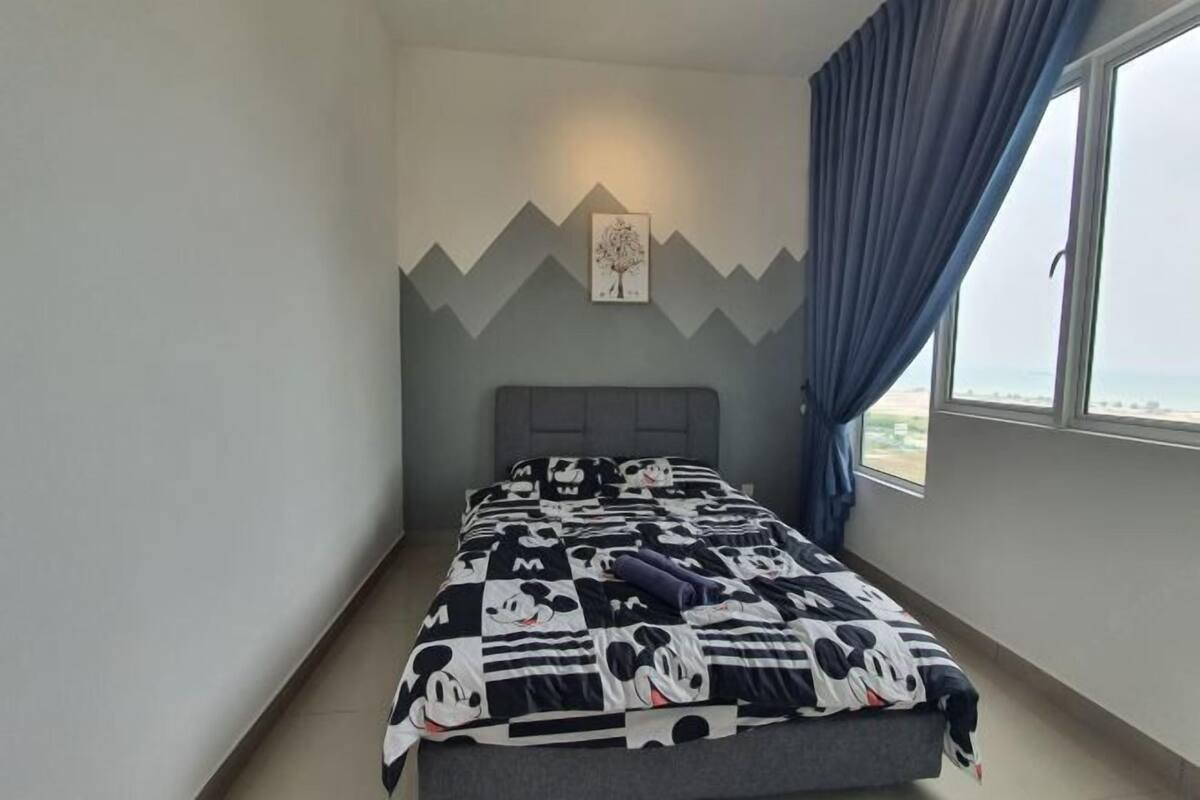 A bedroom with a bed, a window with curtains, a wall-mounted picture, and a mountain design on the wall.
