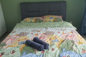 Una cama con una colcha verde y amarilla estampada, un cabecero gris y dos almohadas con diseño de rana.