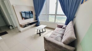A living room with a sofa, a coffee table, a TV mounted on the wall, and a large window with curtains. - Amber Cove Melaka Sea view town (Melaka Tengah)