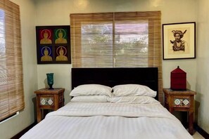 Ein Schlafzimmer mit einem Bett, zwei Nachttischen, einem Fenster mit Jalousien und Wandbildern.