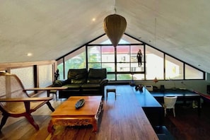 A spacious loft-style room with a high ceiling, a black leather sofa, a wooden coffee table, and a large window providing a view of the outside. - 3 bedroom Penthouse at Asiana Villas in Boracay 5 minutes walk to White Beach (Boracay Island)
